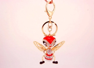 Détail macro du porte-clés abeille dorée avec émail rouge et strass brillants