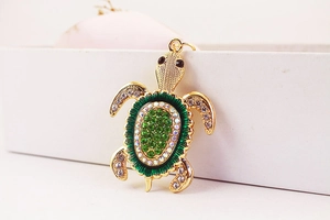 Détail d'un porte-clés tortue doré avec des strass verts et finition en émail