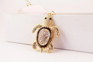 Vue détaillée du pendentif tortue doré orné de strass blancs brillants et scintillants