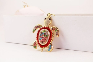 Détail macro d'un porte-clés tortue dorée orné de strass colorés sur une boîte blanche