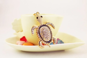 Gros plan d'un porte-clés tortue serti de strass accroché à une tasse de café beige