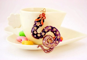 Close-up of a purple rhinestone snake keychain hanging on a white porcelain cup edge
