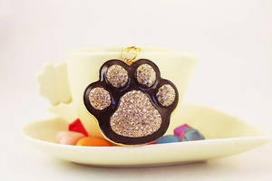 Detail of a black enamel paw print keychain with white crystals on a ceramic cup