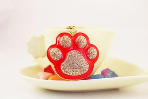 Detail of red rhinestone paw print keychain with gold metal base on a cozy tea cup plate