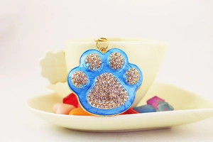 Detail of blue enamel paw charm with white rhinestones on a beige coffee cup