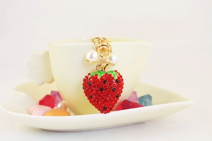 Detail of red rhinestone strawberry keychain with pearls hanging on a white coffee cup