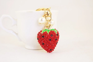 Close-up of strawberry keychain with red rhinestones, green enamel leaves, and white pearls