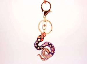 Close-up of cute purple rhinestone snake keychain with gold flower patterns and lobster clasp