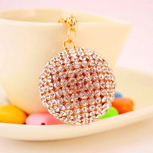 Sparkling crystal ball keychain with gold plating and white rhinestones on white ceramic