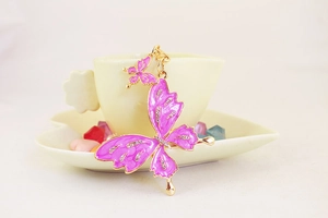 Close-up of pink enamel butterfly keychain with rhinestones hanging on a white cup