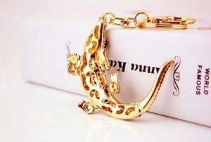 Detail of golden lizard keychain with hollow design and colorful crystals on white background