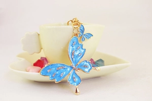 Detail view of sky blue butterfly keychain with rhinestones hanging on a ceramic cup