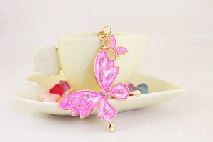 Close-up of pink butterfly keychain with crystals leaning against a cream ceramic cup