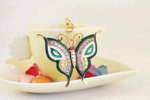 Detail of crystal butterfly keychain with green enamel wings beside a coffee cup