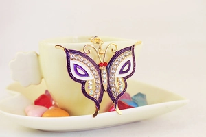 Close-up of a purple rhinestone butterfly keychain on a white coffee cup edge