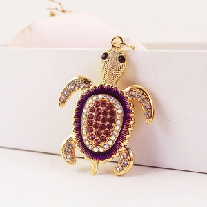 Porte-clés tortue marine dorée orné de strass violets et d'émail sur boîte blanche