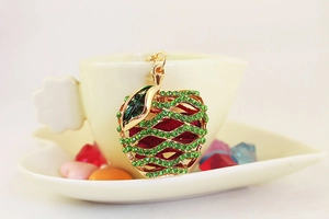 Close-up of apple pendant with green rhinestones and gold frame on a coffee cup