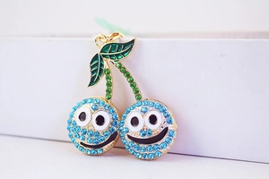 Détail du porte-clés cerise en strass bleus avec visage souriant sur boîte cadeau