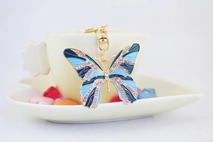 Close-up of elegant blue butterfly keychain with rhinestones on a ceramic cup