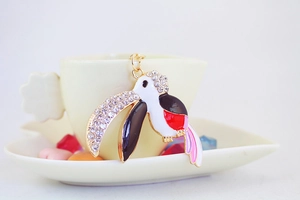 Macro shot of rhinestone parrot pendant on a white coffee cup edge showing enamel detail