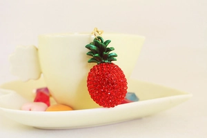 Macro shot of sparkling red rhinestone pineapple keychain hanging on a ceramic cup edge