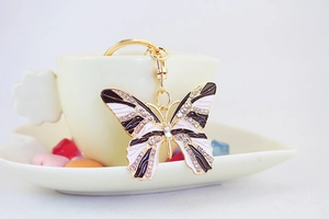 Detail of a gold butterfly keychain with sparkling rhinestones on a cream coffee cup