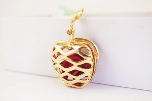 Detail of apple-shaped hollow pendant with red filler and gold-plated mesh texture