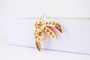 Close-up of gold hollow bird pendant with heart patterns on a white display box