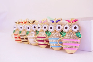 Close-up of owl keychain charms with colorful enamel stripes and sparkling rhinestones