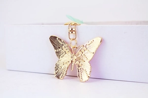 Macro view of gold butterfly keychain featuring intricate textures and rotary metal clasp