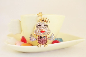 Dettaglio di un portachiavi a forma di pulcino dorato con strass appeso a una tazza