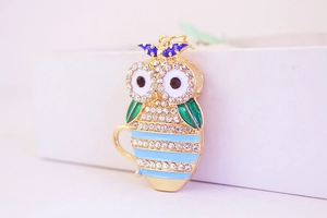 Close-up of owl keychain with golden metal base, blue rhinestones, and green enamel finish