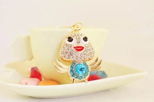 Detail of a gold-plated chick keychain with blue crystal and white rhinestones on a cup
