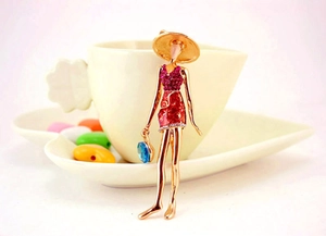 Macro view of rose gold doll brooch featuring pink rhinestones and a blue faceted gem