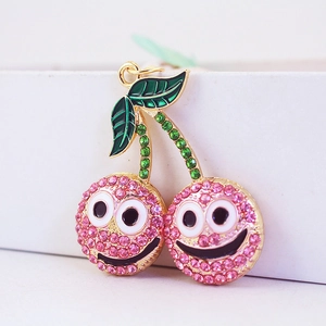 Porte-clés cerise rose avec strass et visages rigolos sur fond de boîte blanche