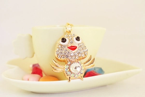 Detail of a gold alloy bird keychain with sparkling crystals leaning on a coffee cup