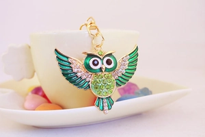 Detailansicht der Eule-Schlüsselanhänger mit grünen Strasssteinen an einer weißen Kaffeetasse