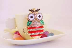 Close-up of owl keychain with white rhinestones and enamel stripes on a tea cup