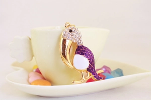 Détail du pendentif toucan avec écailles en émail violet et strass sur une tasse