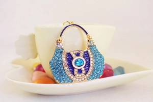 Detailed close-up of a blue rhinestone handbag keychain on a beige coffee cup