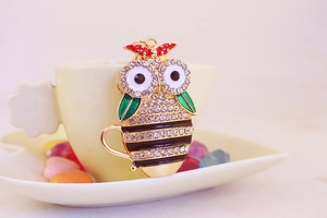 Close-up of owl teacup keychain with sparkling rhinestones and green enamel wings