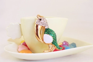 Détail du pendentif toucan en cristal avec émail vert posé sur une tasse beige élégante
