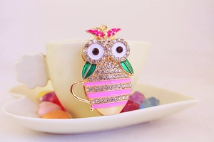 Detail of owl keychain with white rhinestones and pink enamel leaning on a ceramic cup