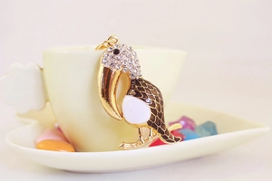 Détail macro du porte-clés toucan avec strass blancs et texture d'écailles en émail