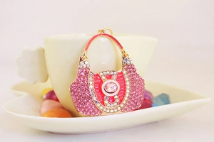Close-up of pink rhinestone handbag keychain resting on a white coffee cup
