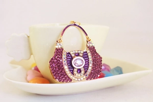 Detailed close-up of a crystal-encrusted purple handbag keychain pendant on a white saucer