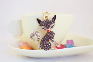Dettaglio del portachiavi a forma di volpe con strass blu poggiato su una tazza