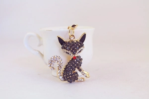 Dettaglio di un portachiavi a forma di volpe dorata con strass bianchi e neri su una tazza