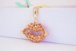Detail shot of golden metal lip keychain with mesh design on white display stand