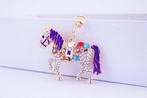 Detail of horse keychain with colorful gemstones and purple enamel mane on gold metal